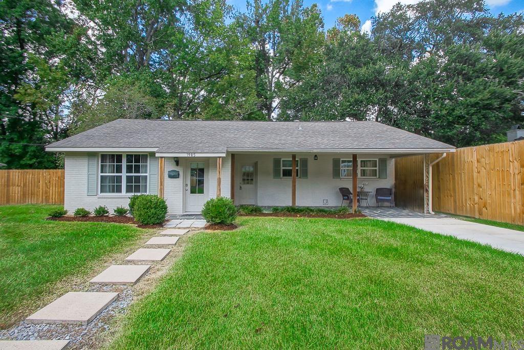 White single-story ranch house with a covered porch, stepping-stone path, and fenced green lawn.