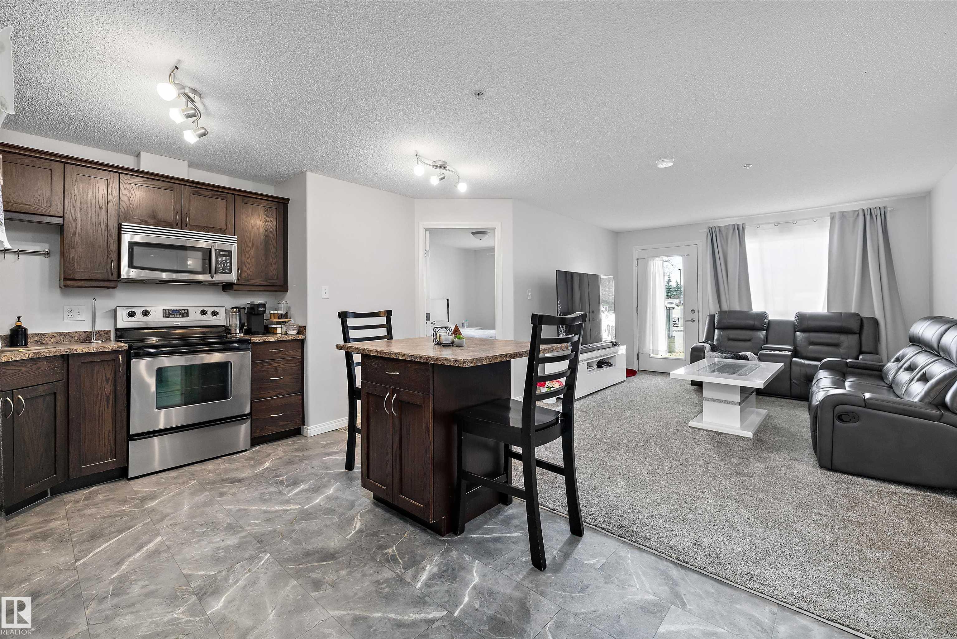 Experience effortless urban living in this pristine apartment-style condo, perfectly situated just steps away from the LRT, local restaurants, and premier shopping destinations. This exceptional unit truly shines with brand-new carpet and fresh professional paint throughout, standing out as one of the most meticulously maintained units in the entire condo. The functional floor plan offers two spacious bedrooms and two full bathrooms, centered around a stylish dark maple kitchen featuring a social island and stainless steel appliances. A bright, open-concept living area creates a welcoming atmosphere, complemented by a laundry room for added convenience. This home includes a titled parking stall and access to the building's private exercise room. With its spotless condition and unbeatable proximity to major amenities, this property represents incredible value in a vibrant community. Whether you are a first-time buyer or looking to downsize, this move-in-ready opportunity is a must-see!
